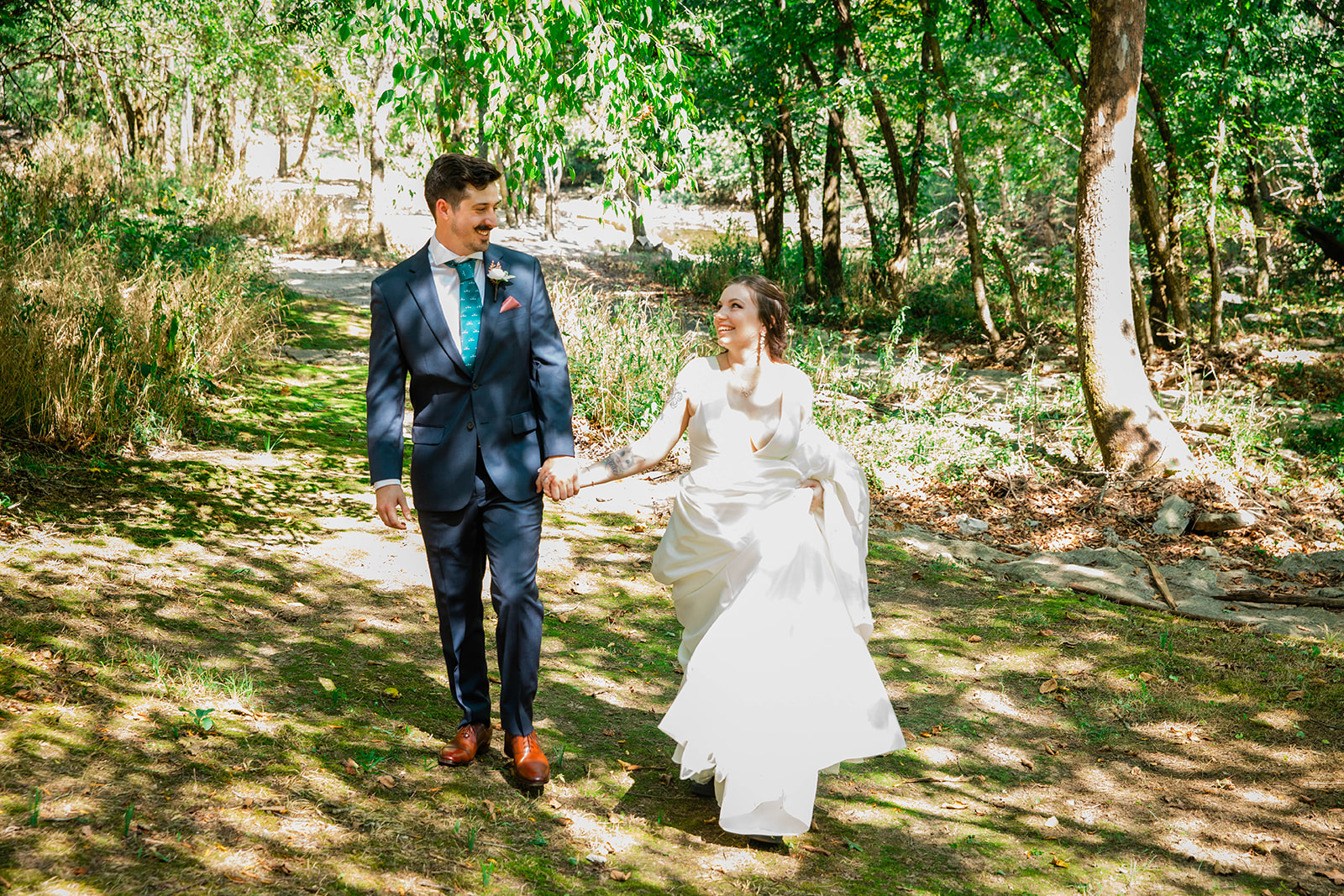 bride and groom holding hands walking through woods